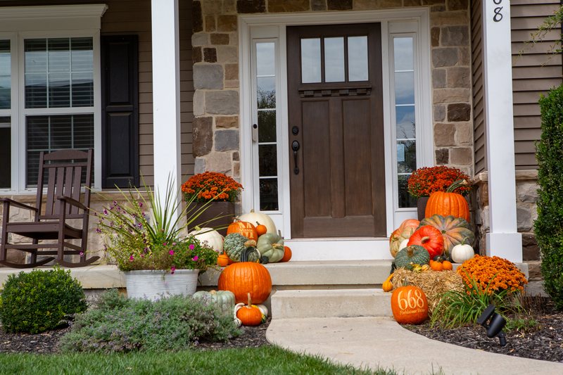 The Harvest close on the front door, pumpkins in orange, white and sage green either side, a straw bale carrying an engraved house-number pumpkin