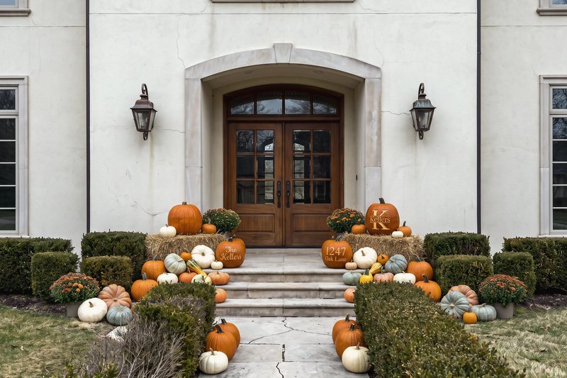 The Estate on a cream stucco house with an arched entry, filling the limestone landing on two straw bales, down both sides of the steps and along both edges of the walk with mums, gourds and three engraved pumpkins