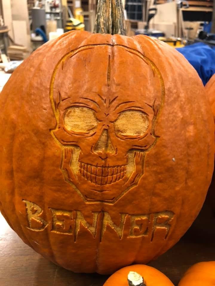 A pumpkin laser-engraved with a skull and the family name Benner, on a workbench in the workshop