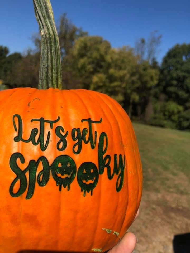 A pumpkin laser-engraved with the script words Let&rsquo;s get spooky, outdoors under a blue sky