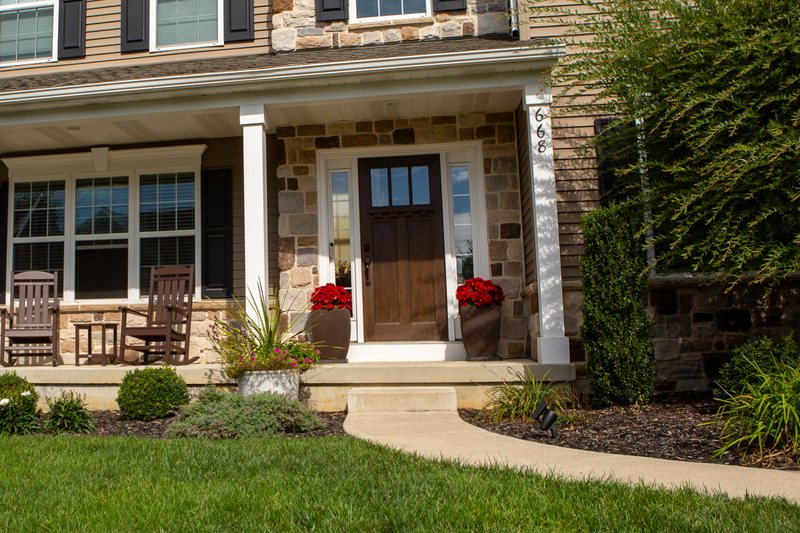 The Signature Porch on a stone-front colonial before the pumpkins arrived, two rocking chairs on the deck