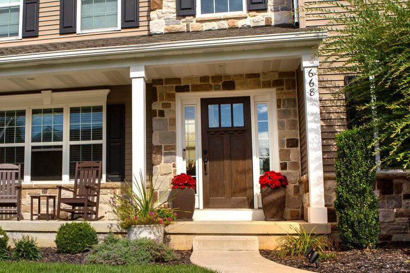 The same stone-front colonial porch before the pumpkins arrived, two rocking chairs on the deck
