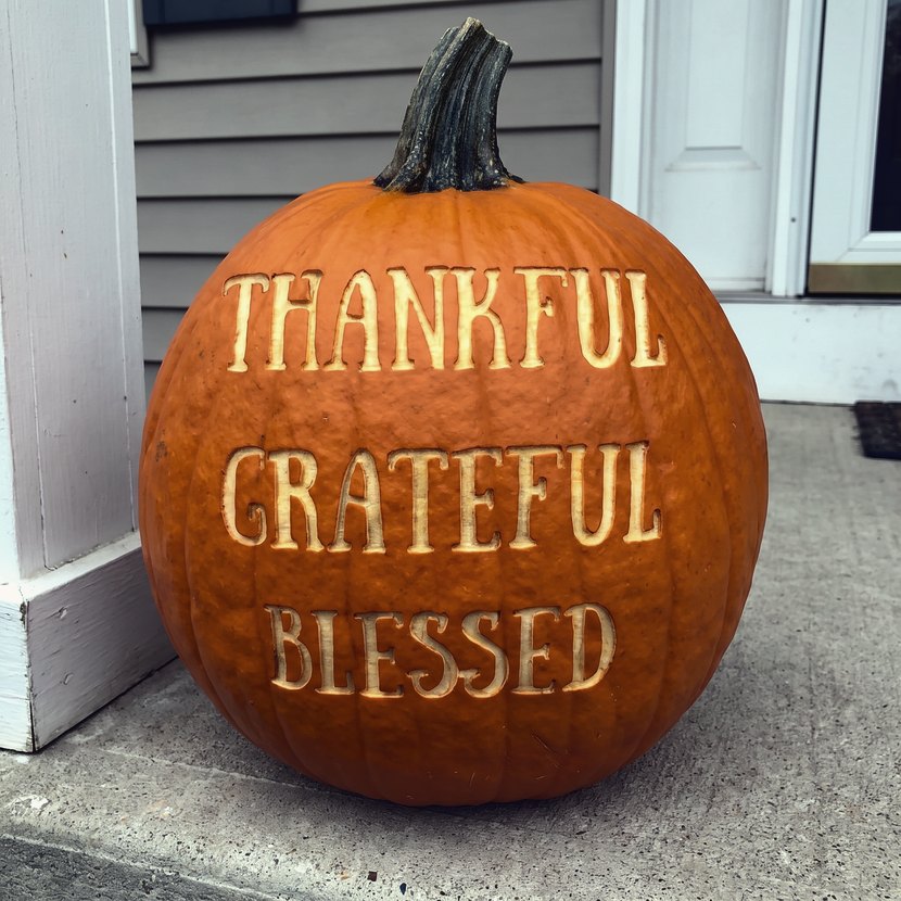 A pumpkin laser-engraved with the words Thankful, Grateful, Blessed, sitting on a porch deck